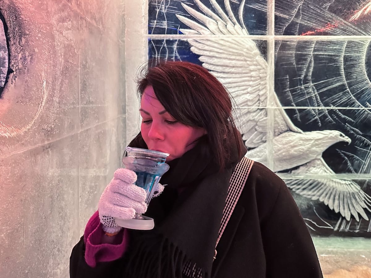 a woman drinking a blue cocktail in a glass of ice in an ice bar