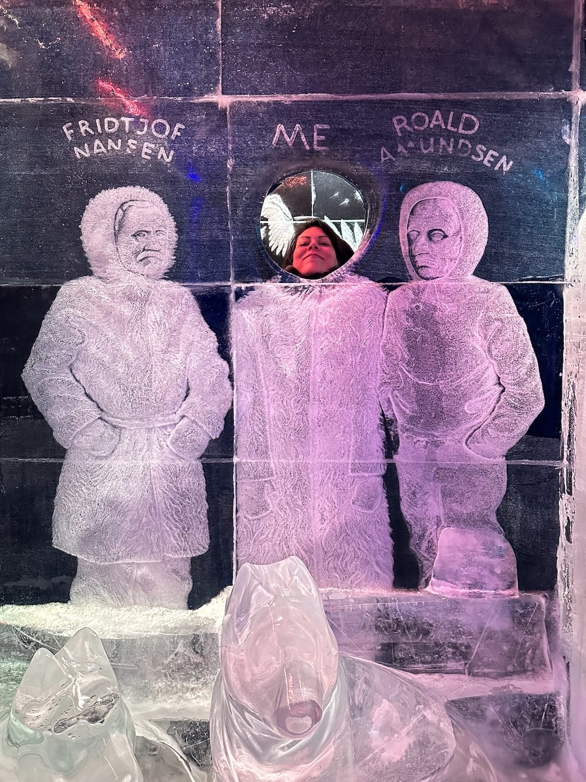 a woman putting her head in a cutout of ice next two two polar explorers